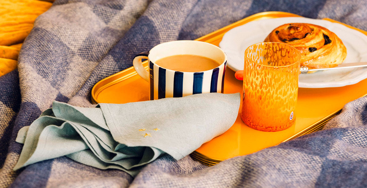 Breakfast in bed with mug of tea, glass of orange juice and croissant on orange serving tray