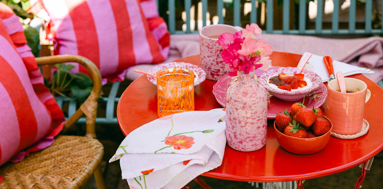 Strawberries and cream on small red garden table with pink mugs and bowls