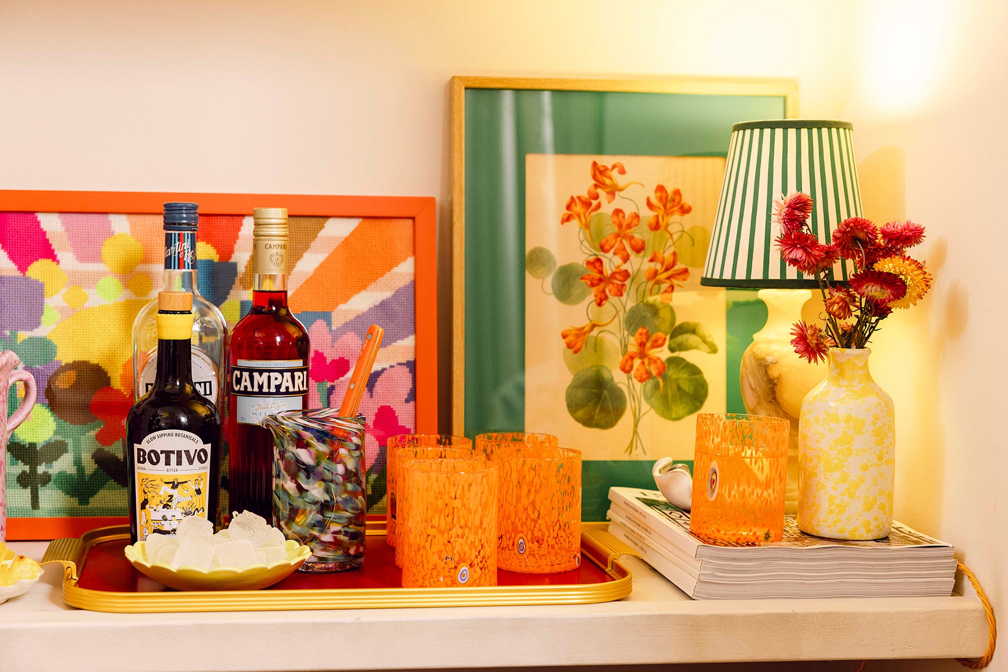 Drinks corner with bottles of spirits, orange tumblers, stripy lampshade and framed artwork