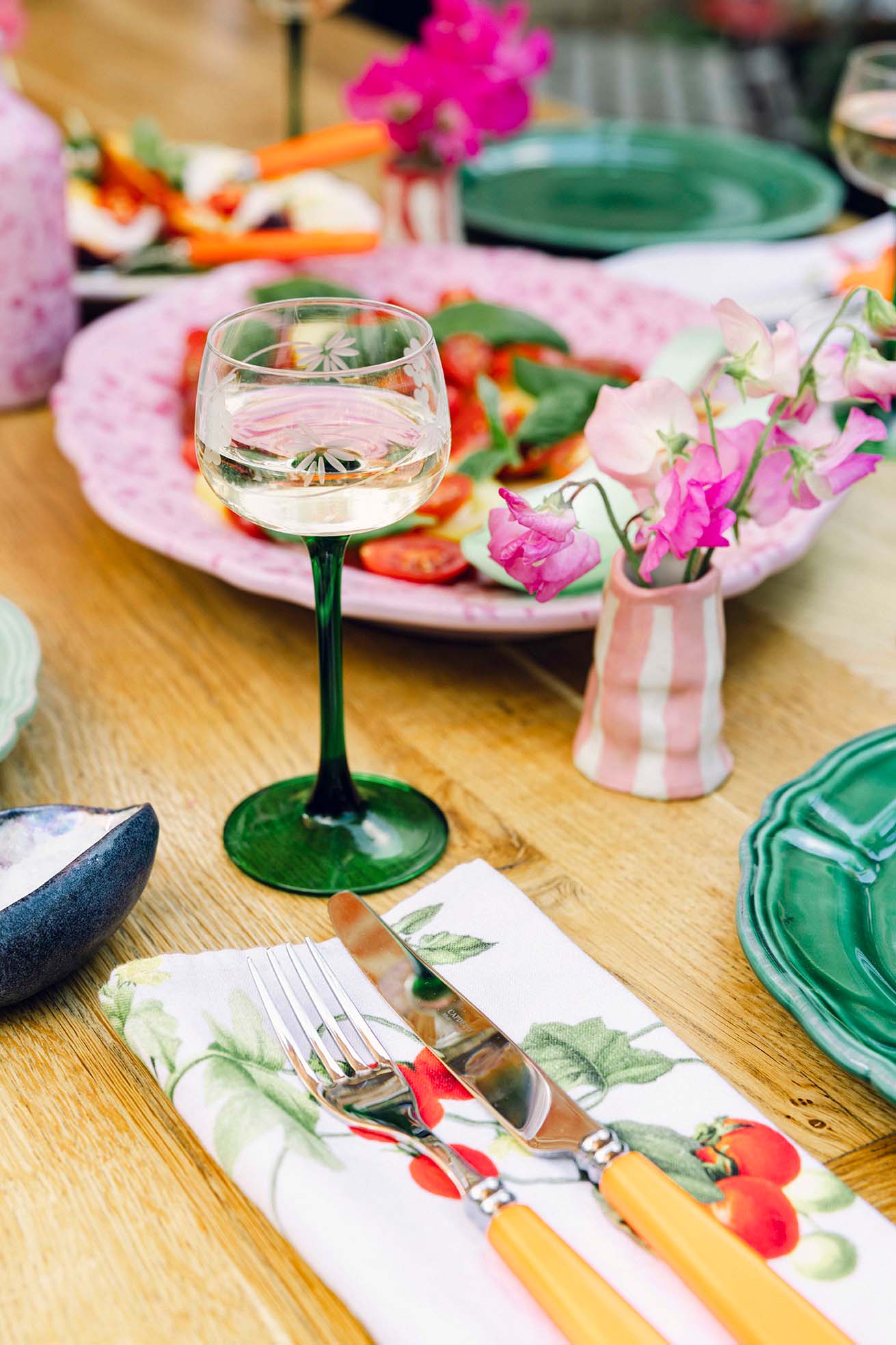 Garden table summer salad with vintage wine glass, yellow cutlery and floral napkin